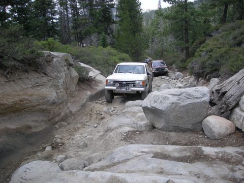 1991 Ford Bronco - Multiple vehicles traverse a challenging rocky path in a wooded area.