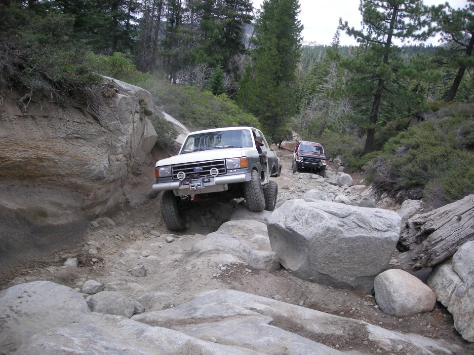 White 1991 Ford Bronco navigating a rocky off-road trail with another vehicle behind
