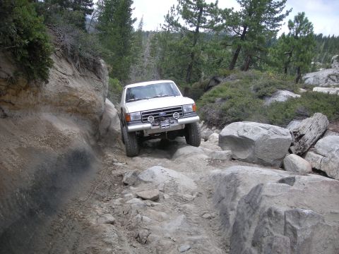 1991 Ford Bronco - White 1991 Ford Bronco tackling a challenging off-road path with large boulders.