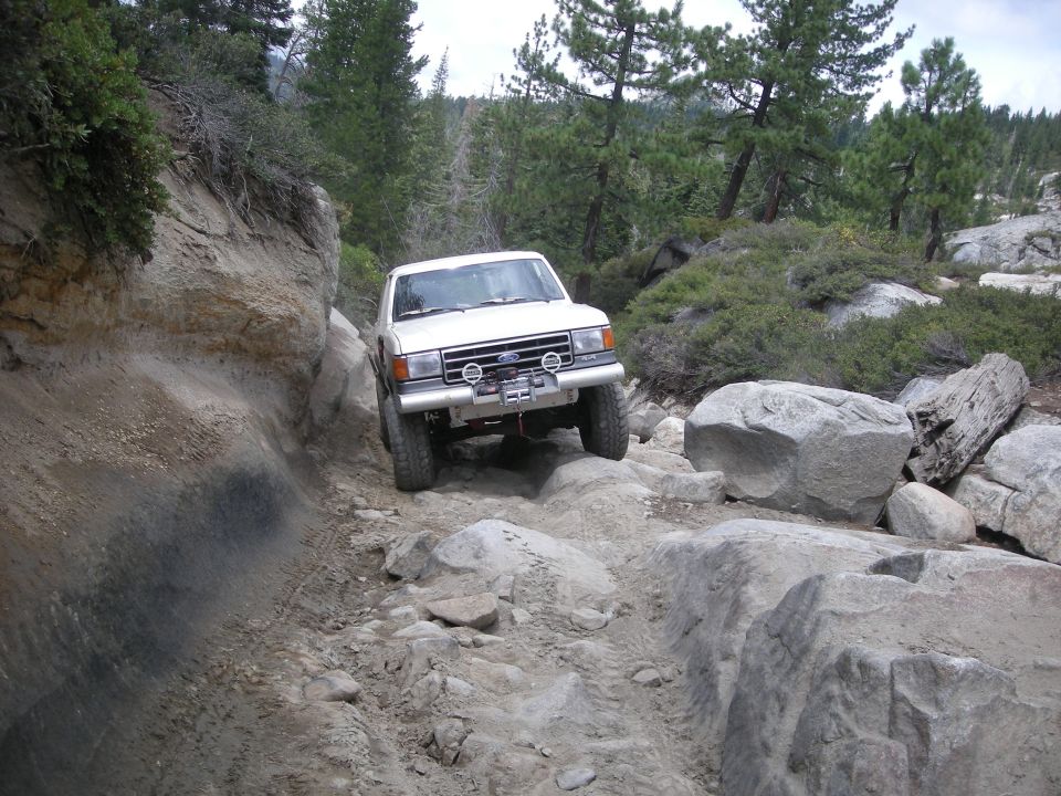 1991 Ford Bronco navigating a difficult rocky trail with steep dirt banks