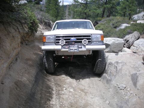 1991 Ford Bronco - This white Ford truck navigates a challenging rocky off-road path.