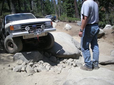 1991 Ford Bronco - A man watches a Ford F-Series truck traverse a challenging rock obstacle off-road.