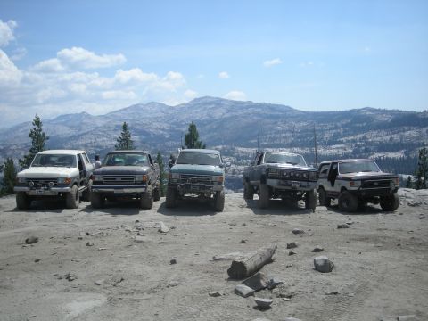 1991 Ford Bronco - A group of off-road vehicles, including a 1991 Ford Bronco, are parked on a rocky terrain with a scenic mountain backdrop.
