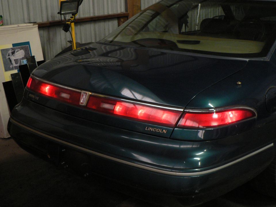 Rear end of a dark green Lincoln coupe with lit taillights