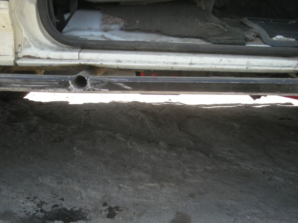 Side view of a vehicle's undercarriage, showing the door sill and a metal tube rock slider welded on. The interior carpet is visible through the open door