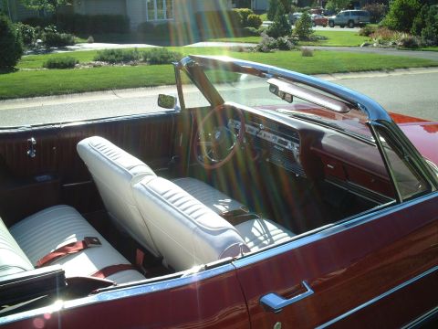 1967 Ford Galaxie - The interior of a classic red convertible shows white bucket seats and a dashboard with wood-grain accents.