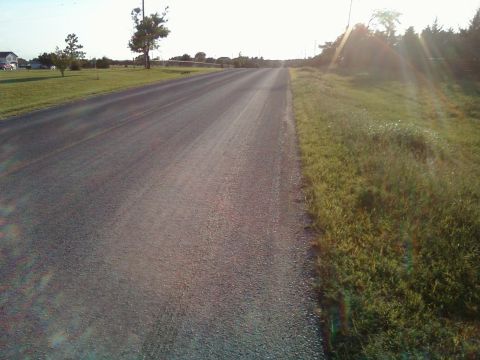 2000 Mercury Grand Marquis - A long, empty road stretches into the distance under a bright sky, bordered by grassy fields.