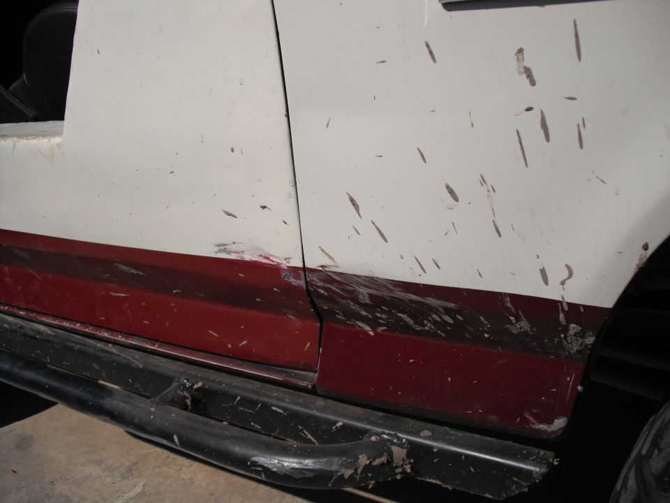 Side of a white and maroon vehicle with black rock sliders, covered in mud splatters