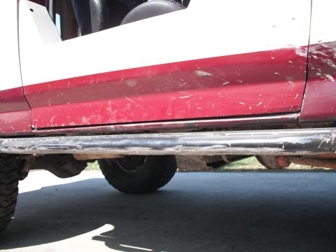 1991 Ford Bronco - The side view of a red and white SUV reveals its running boards and lower body panels.