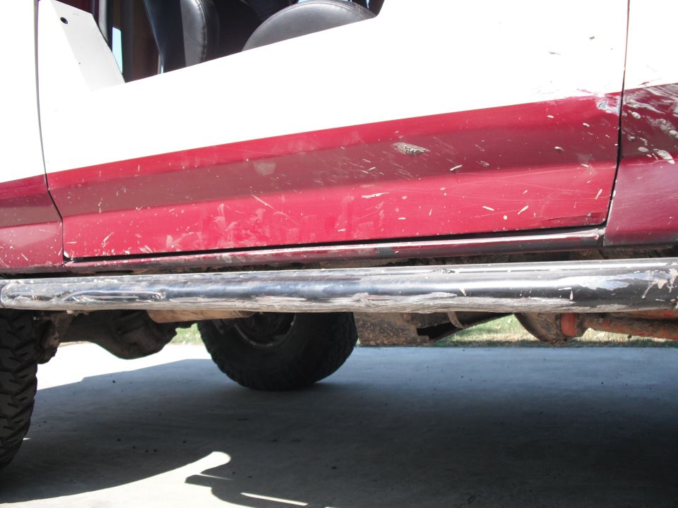 Red and white SUV side panel with black running boards, showing mud splatter and scratches