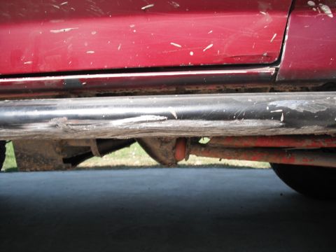 1991 Ford Bronco - Close-up view of the lower side panel and running boards of a red vehicle, showing suspension components underneath.