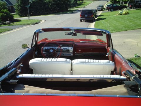 1967 Ford Galaxie - The interior of a red 1967 Ford Galaxie convertible is visible, with white seats and a red dashboard.