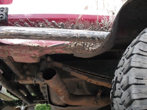 1991 Ford Bronco - The vehicle's lower body and suspension components are heavily coated in dried mud, indicating recent off-road use.
