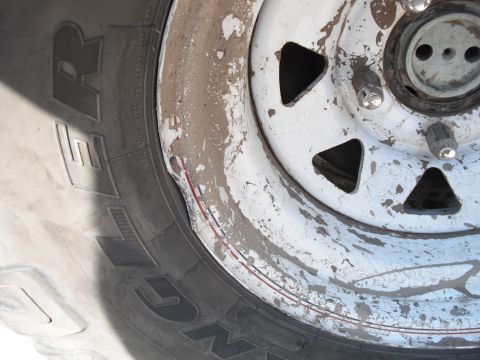1991 Ford Bronco - Close-up of a damaged white steel wheel and tire, with visible chipping and a dent in the rim.