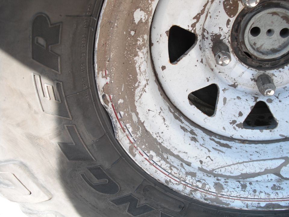 Damaged white steel wheel with tire, showing chipped paint and a dented rim