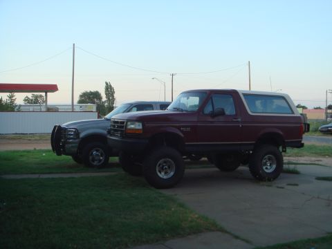 1992 Ford Bronco - A lifted maroon 1992 Ford Bronco is parked next to a silver truck under a clear sky.
