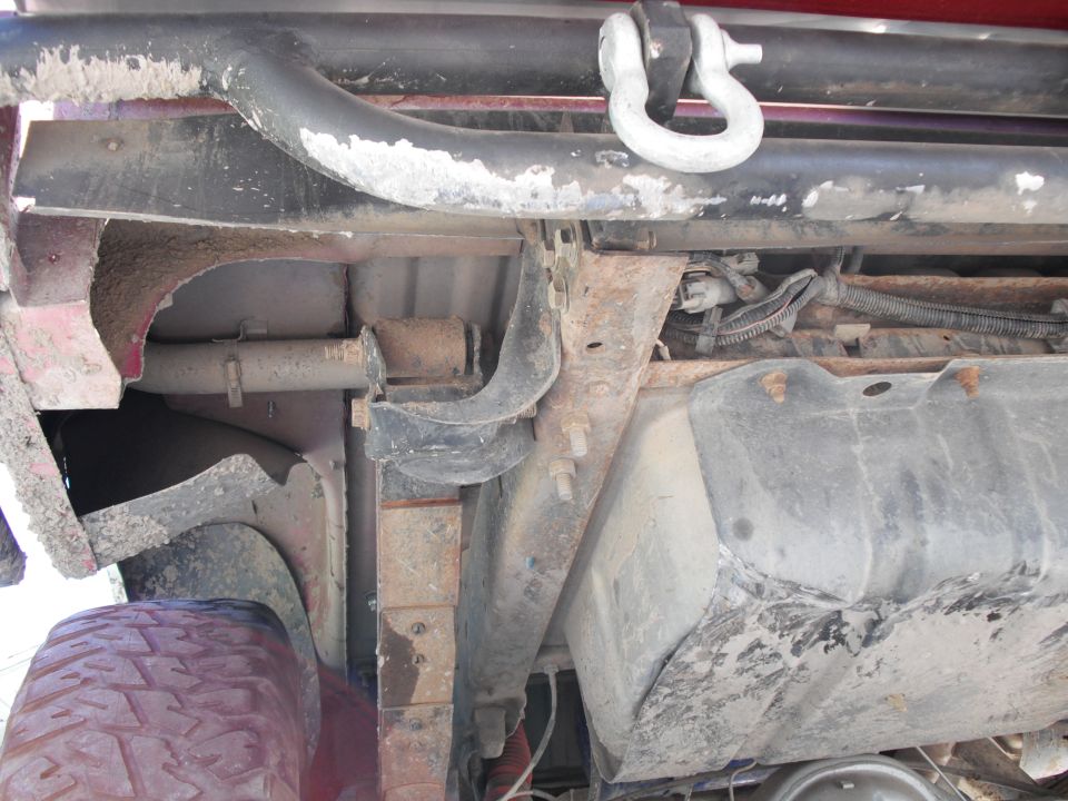 Undercarriage view showing suspension, fuel tank, and a tow shackle on a red vehicle