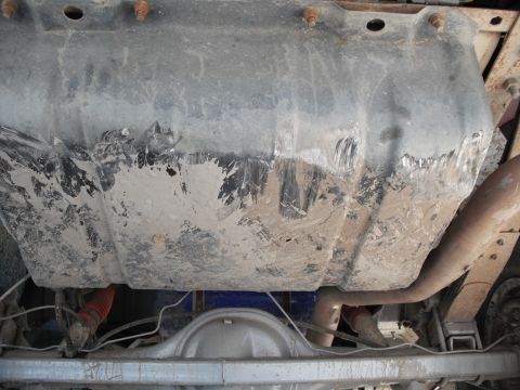 1991 Ford Bronco - The underside of a vehicle shows a heavily soiled fuel tank and exhaust components.