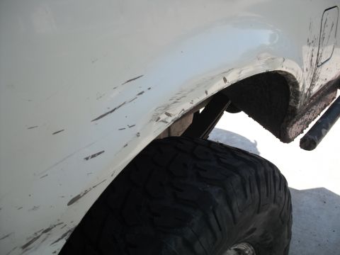 1991 Ford Bronco - Close-up of a dirty white SUV fender and tire, with visible scratches on the bodywork.