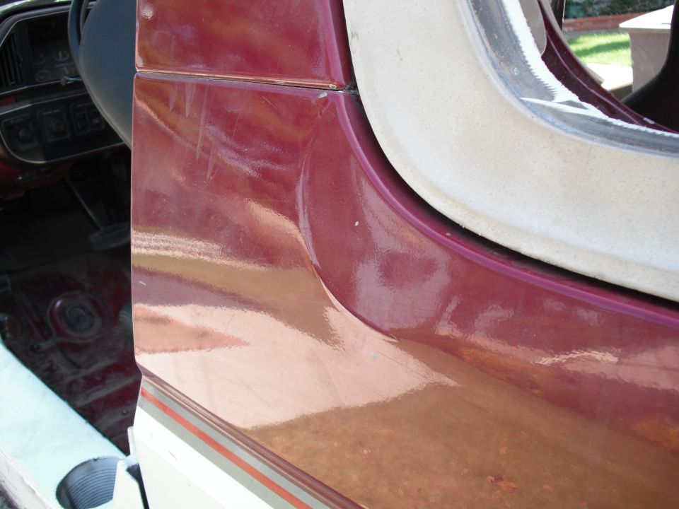 Maroon door jamb with scuff marks and beige trim. Interior floor visible with red carpet and gas pedal