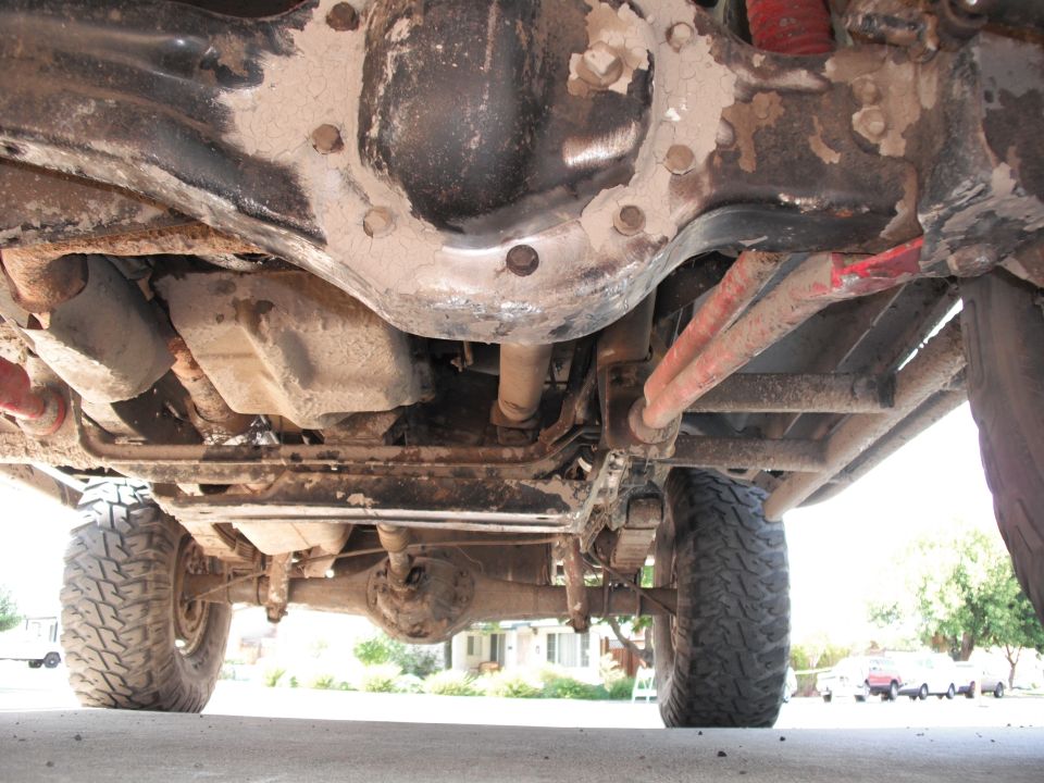 Undercarriage of a lifted off-road vehicle showing suspension, drive shaft, and tires