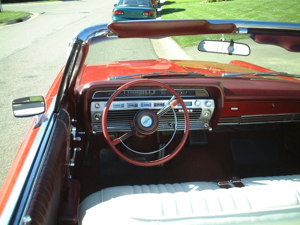 Red convertible interior with red steering wheel, chrome dash, and white seats, top down.