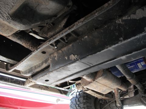 1991 Ford Bronco - The undercarriage of a vehicle shows its frame, exhaust system, and a portion of a tire.