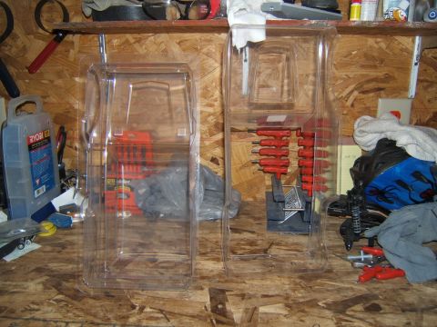1988 Ford Bronco - Two clear plastic packages with RC car parts are displayed on a workbench, with tools and other items in the background.