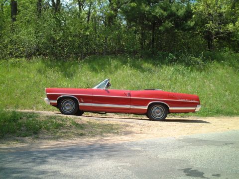 1967 Ford Galaxie - A red 1967 Ford Galaxie convertible is parked on the side of a road with trees and grass in the background.