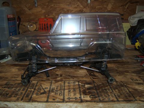 1988 Ford Bronco - A clear body shell for an RC crawler sits atop its chassis on a wooden surface.