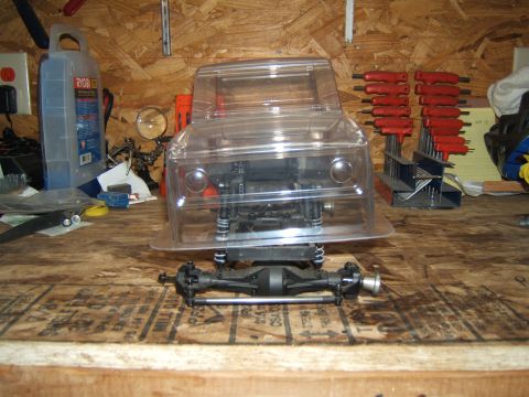 1988 Ford Bronco - An unassembled RC car chassis and body sit on a workbench next to tools and supplies.