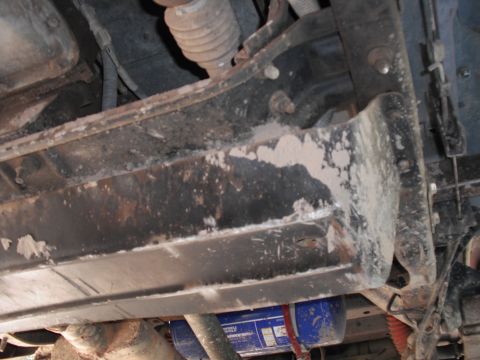 1991 Ford Bronco - The undercarriage of a vehicle is visible, a blue oil filter and heavily weathered frame components.