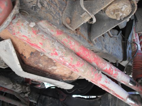 1991 Ford Bronco - The undercarriage of a vehicle reveals heavily used suspension parts with chipped red paint and accumulated grime.