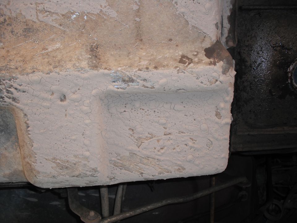 Underbody of a vehicle with white coating and dark components visible