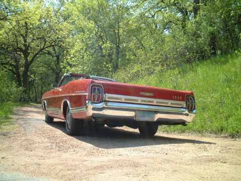 1967 Ford Galaxie - The rear of a red 1967 Ford Galaxie convertible is shown on a dirt road with trees and grass in the background.