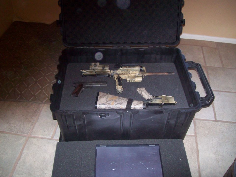 Case with a disassembled rifle and a pistol inside, resting on a laptop