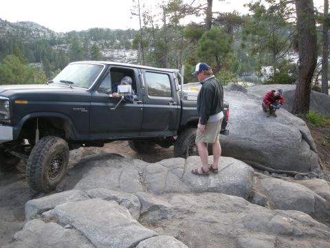 1991 Ford Bronco - A lifted Ford F-Series truck navigates a rocky terrain, with people observing the off-road challenge.