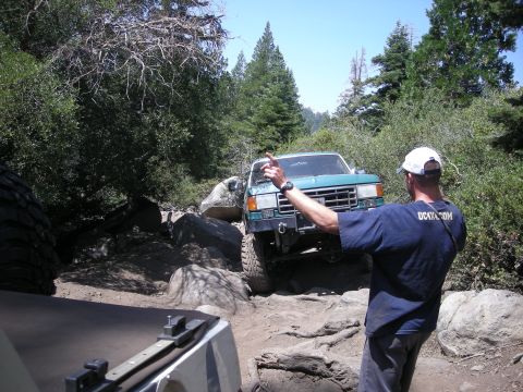 1991 Ford Bronco - A teal 1991 Ford Bronco navigates a challenging rocky trail with a driver giving directions.