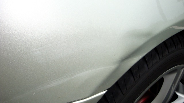 Crease dent and scuff in silver body panel above wheel arch