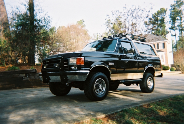 Black Ford Bronco SUV with brush guard and roof light bar parked in a driveway