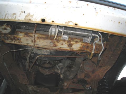 1996 Ford Bronco - The underside of a vehicle reveals a corroded radiator and various hoses and metal components.