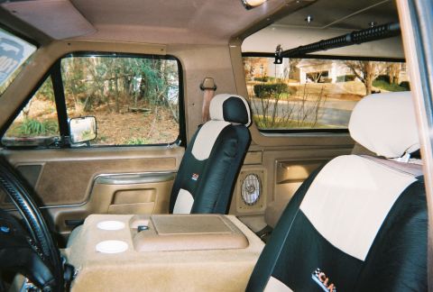 1990 Ford Bronco - The interior of the vehicle shows tan door panels and a center console with cup holders.