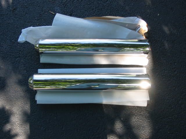Two chrome exhaust tips on white tissue paper on asphalt