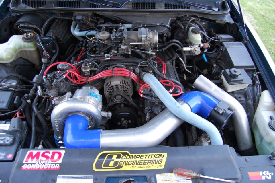 Engine bay with a large turbocharger and blue intake piping, plus MSD and Competition Engineering stickers
