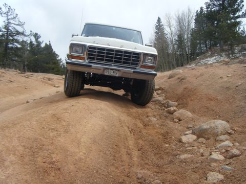 1979 Ford Bronco - A 1979 Ford Bronco navigates a rocky, off-road trail under a cloudy sky.