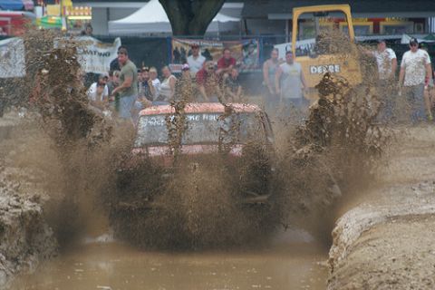2005 Ford Excursion - A red SUV navigates a muddy obstacle course, with a yellow John Deere tractor visible behind the spectators.