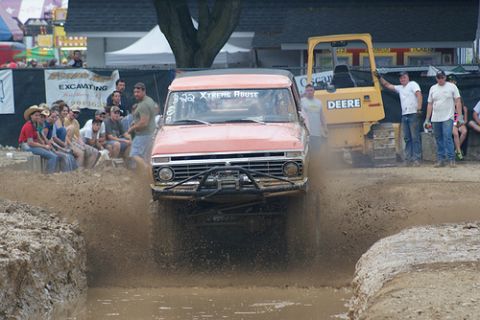 2005 Ford Excursion - Pickup truck navigates a mud bog with spectators watching and a bulldozer nearby.