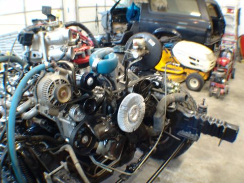 1996 Ford Bronco - Engine assembly in a garage with a dark SUV and lawnmowers in the background.