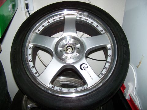 1997 Mitsubishi Eclipse - A close-up of a silver alloy wheel with a black tire, a "G-Racing" logo and visible lug nut holes.