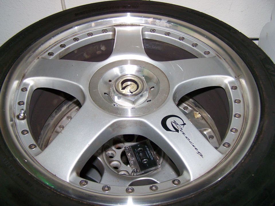 Silver five-spoke aftermarket wheel with black racing logo and cassette tape inside
